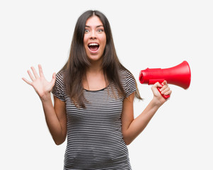 Young hispanic woman holding megaphone very happy and excited, winner expression celebrating victory screaming with big smile and raised hands