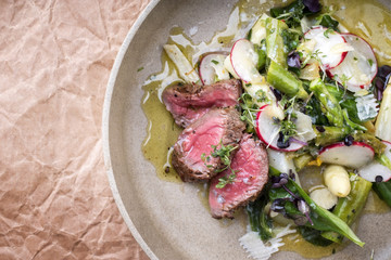 Traditioneller Frühlingssalat mit gegrillten dry aged  Rinderfilet Steak aufgeschnitten und grünen und weißen Spargel als Draufsicht auf einem Teller mit Textfreiraum links 