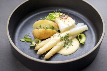 Modern German fried cod fish filet with white asparagus in hollandaise sauce und roast potatoes as top view on a plate