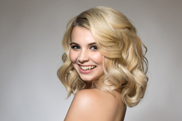 Blonde with curls on a gray background, natural make-up and clean skin. beautiful smile and big...
