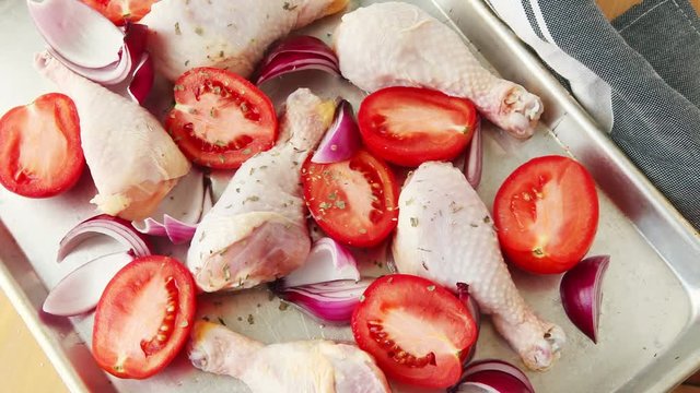 Woman cook sprinkles dried basil, thyme and oregano over a chicken sheet pan dinner with tomatoes and onion