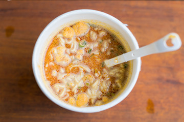 Cup of instant noodle Tom Yum Kung Flavor with plastic fork on wooden table