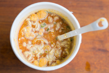 Cup of instant noodle Tom Yum Kung Flavor with plastic fork on wooden table