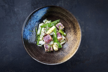 Modern style fried tuna fish tataki filet salad with white asparagus sugar snaps and parmesan cheese as top view on a plate with copy space