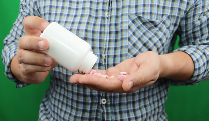 Mans hands with pills on, spilling pills out of bottle on green background