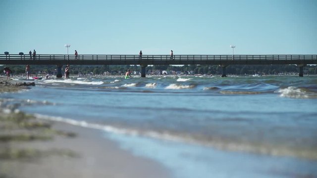 Rippling waves crash onto shore in front of active pier 4K