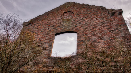 A derelict red brick building in a forest.