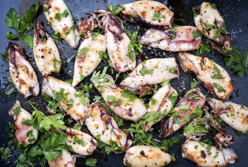 Traditional barbecue Greek calamari with herb and spices as top view on a black metal sheet