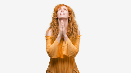 Young redhead woman begging and praying with hands together with hope expression on face very emotional and worried. Asking for forgiveness. Religion concept.