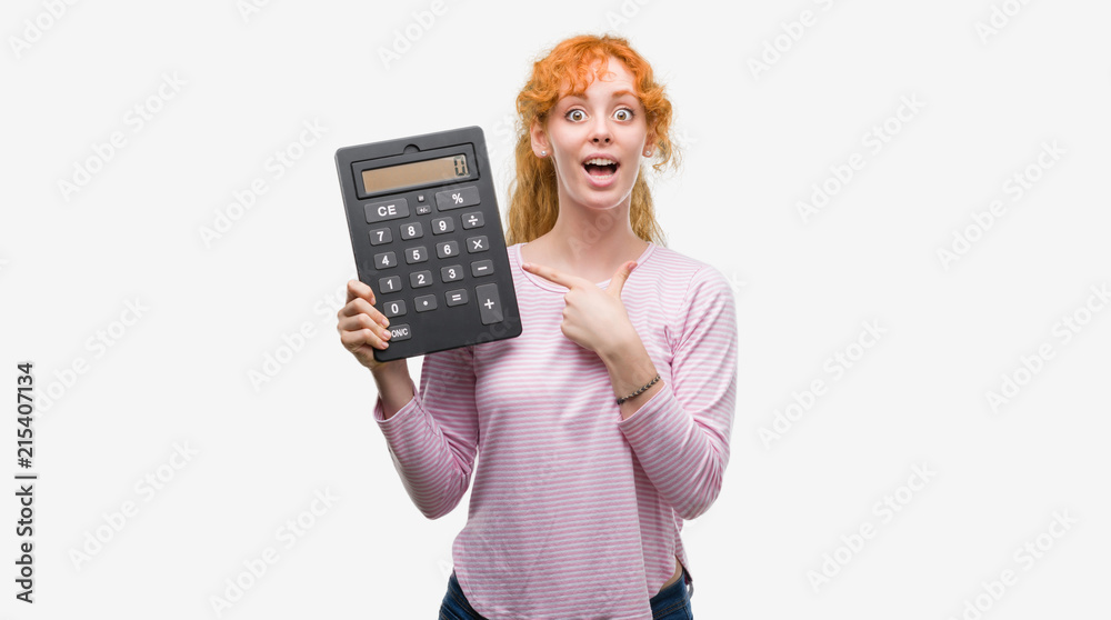 Poster young redhead woman holding big calculator very happy pointing with hand and finger