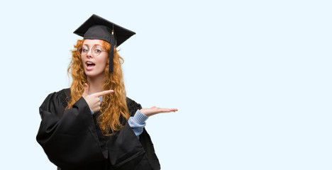 Young redhead student woman wearing graduated uniform very happy pointing with hand and finger