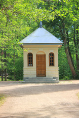 Small Booth House in the Park with Green Trees Nature on Background. Summer View of Narrow Alley Leading to Cabin in the Woods on Sunny Summer Day.