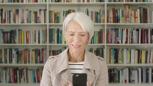 Portrait elderly woman student using smartphone research bookshelf library university