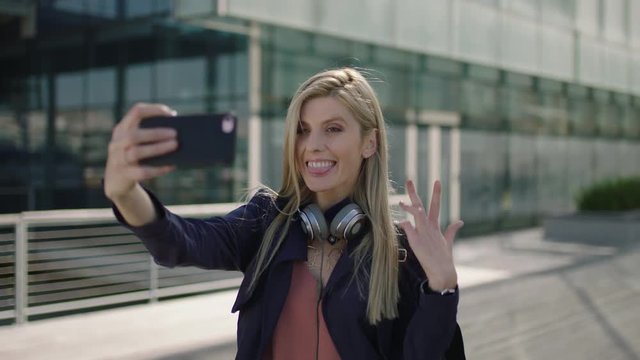 portrait of young lively blonde business woman intern smiling posing taking selfie photo using smartphone camera in city