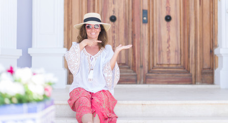 Middle age brunette woman wearing summer hat on vacations very happy pointing with hand and finger