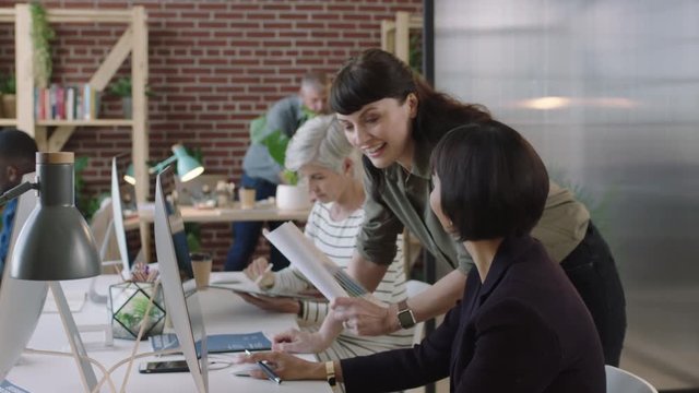 senior mixed race business woman using computer in modern office young female intern showing chart data pointing at screen diverse team collaborating in workspace
