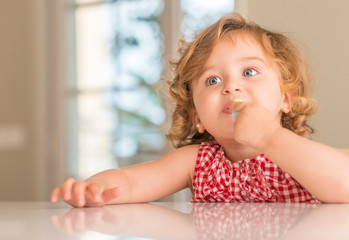 Beautiful blonde child with blue eyes eating candy at home.