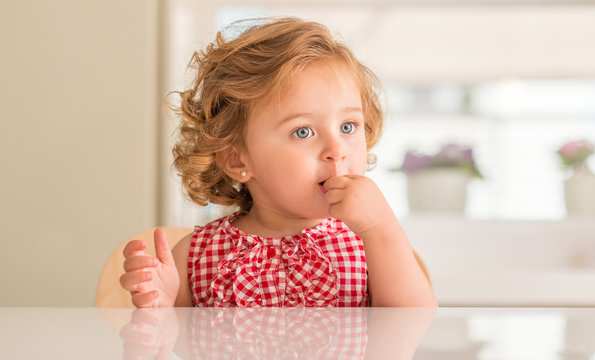 Beautiful blonde child with blue eyes eating candy at home.