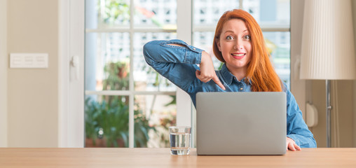 Redhead woman using computer laptop at home with surprise face pointing finger to himself
