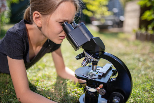 Ein 9 jähriges Mädchen liegt auf dem Rasen im Garten und schaut in das Okular eines Mikroskops.