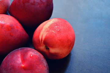 Ripe red peaches and nectarines with water drops on dark wooden background.
