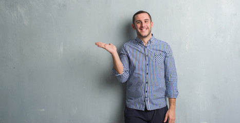 Young caucasian man over grey grunge wall smiling cheerful presenting and pointing with palm of...