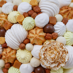 A lot of different sweets, such as: marshmallows, sweets, chocolate, biscuits and meringue in the form of carnation as a background or a backdrop