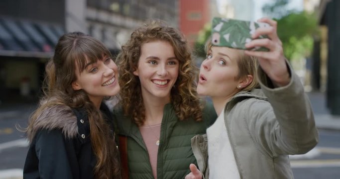 portrait young group of friends taking selfie photo using smartphone mobile camera technology enjoying fun making faces together in city street background slow motion