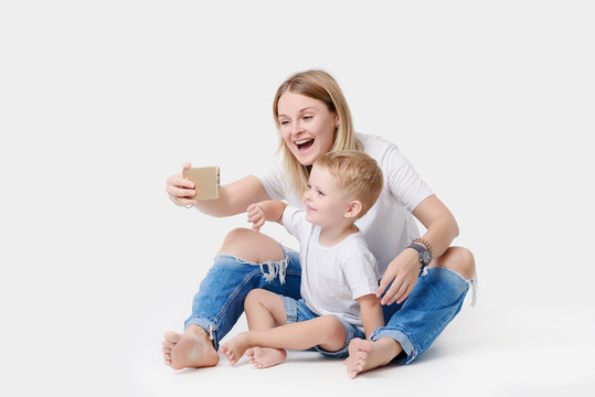 Happy young mother playing with her young son on a white isolated background. Take pictures and videos on your mobile phone, make selfie