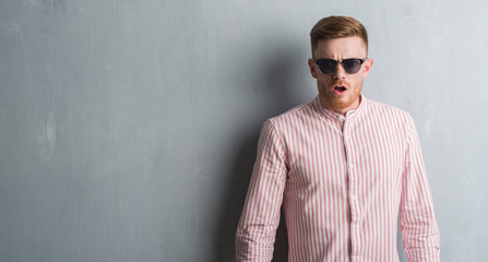 Obraz premium Young redhead man over grey grunge wall wearing sunglasses scared in shock with a surprise face, afraid and excited with fear expression