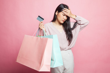 Unhappy  young Asian woman with shopping bags and credit card.