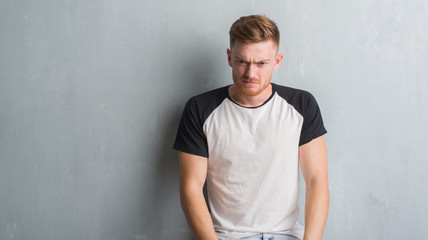 Young redhead man over grey grunge wall depressed and worry for distress, crying angry and afraid. Sad expression.