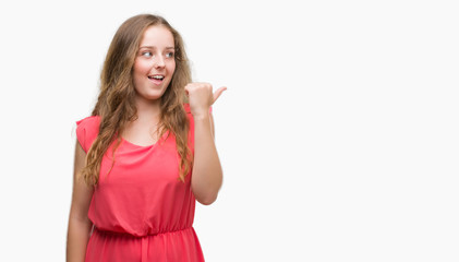 Young blonde woman wearing pink dress pointing and showing with thumb up to the side with happy face smiling