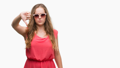 Young blonde woman wearing pink sunglasses with angry face, negative sign showing dislike with thumbs down, rejection concept