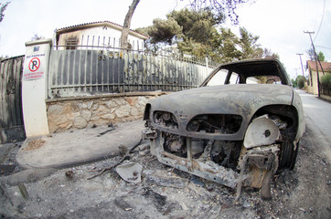 Fototapeta premium After firestorm phenomenon in Greece Burnt down car on road. Burnt tire and molten metal