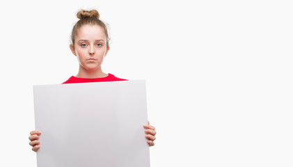 Fototapeta premium Young blonde woman holding advertising banner with a confident expression on smart face thinking serious