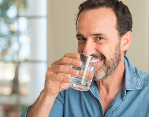 Fototapeta na wymiar Middle age man drinking a glass of water with a happy face standing and smiling with a confident smile showing teeth