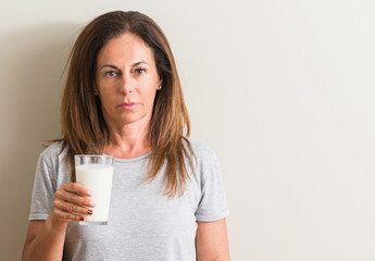 Middle age woman drinking a glass of fresh milk with a confident expression on smart face thinking...