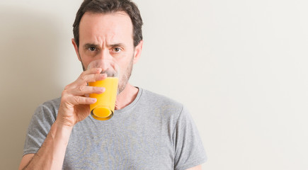 Fototapeta premium Senior man drinking orange juice in a glass with a confident expression on smart face thinking serious