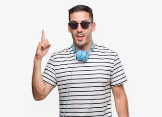 Handsome young man wearing headphones pointing finger up with successful idea. Exited and happy. Number one.