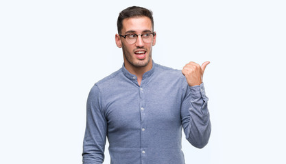 Handsome young elegant man wearing glasses smiling with happy face looking and pointing to the side with thumb up.