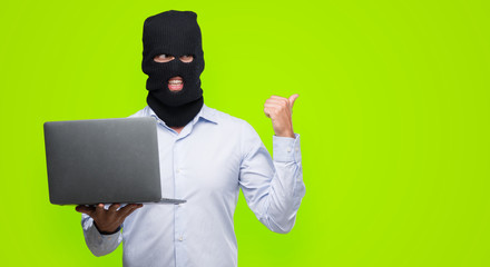 Business hacker man holding a computer laptop pointing with hand and finger up with happy face...