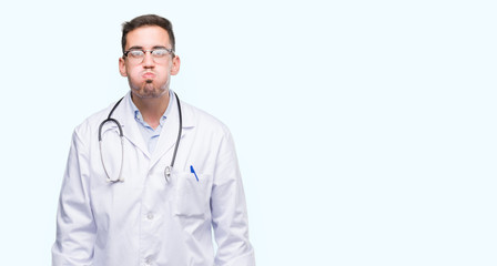 Fototapeta premium Handsome young doctor man puffing cheeks with funny face. Mouth inflated with air, crazy expression.