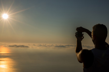 Handsome man taking photograph of a sunset above the clouds