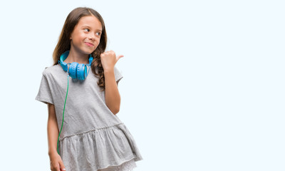 Brunette hispanic girl wearing headphones pointing and showing with thumb up to the side with happy face smiling