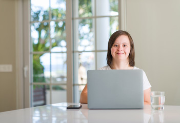 Down syndrome woman at home using computer laptop with a happy face standing and smiling with a...