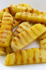 Grilled pineapple wedges on a white plate, closeup. Summer food. Side view.