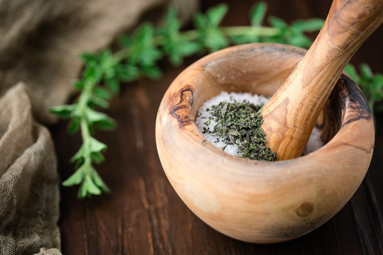 Dried Oregano in Mortar and Pestle to make Herb Salt with a fresh sprig of Oregano on a Wooden Table