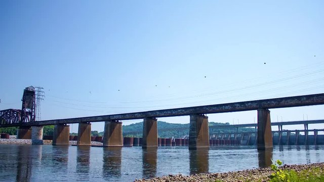 Time lapse of river moving past lock and dam and underneath a train trestle.