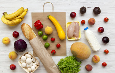 Variety of healthy food with paper bag on white wooden table. Cooking food background. Flat lay of fresh fruits, veggies, greens, meat, milk. Top view, overhead, from above. Shopping concept.